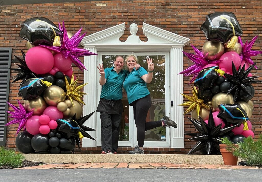 Custom graduation balloon towers with black, pink, and gold balloons, chrome starbursts, and black graduation cap foil balloons for front porch graduation party decor. Organic balloon columns by Party Perks in St. Louis. Luxury balloon styling for graduation celebration, best graduation balloons near me, outdoor graduation decor St. Louis.and the best balloon decor in St. Louis. Graduation decor for parties, custom balloon installation, in Ladue, MO