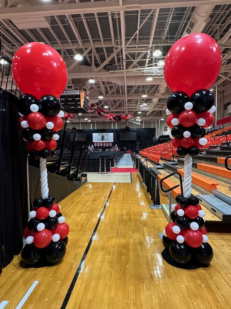 Two large red, black, and white balloon columns with oversized toppers flank a gymnasium entrance at a back to school event in St. Louis.