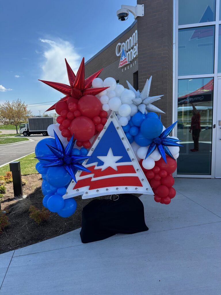 Organic red, white, and blue balloon garland with metallic starbursts framing a company logo, created by Party Perks STL at a St. Louis credit union event.