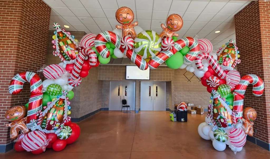 Oversized gingerbread-themed balloon arch with candy canes and gingerbread men — Christmas balloon installation by Party Perks