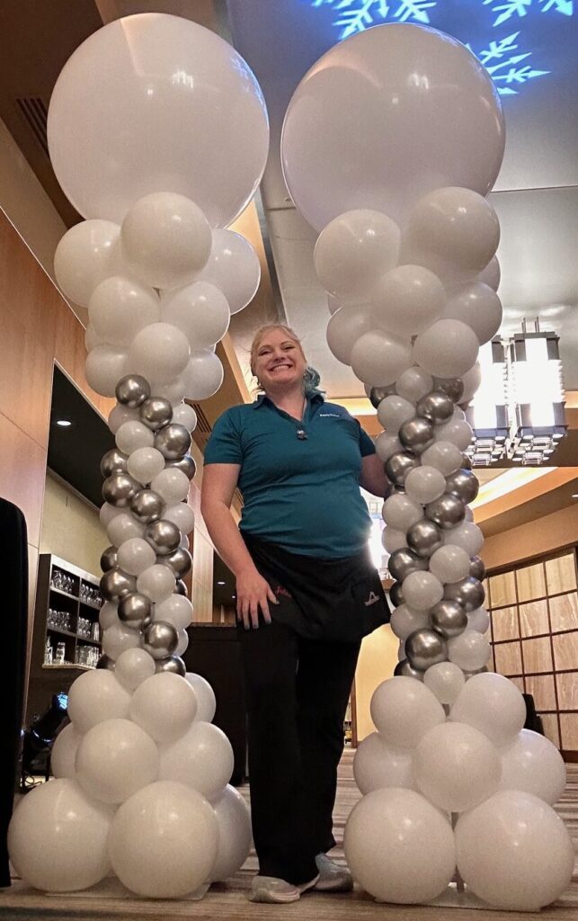Pair of white and silver Roman balloon columns with oversized white balloon toppers, installed indoors for a winter-themed event.