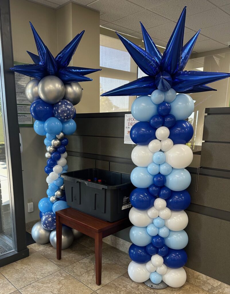 Blue and white balloon columns with metallic blue starburst toppers and silver accent balloons, installed inside a lobby entrance for an event.