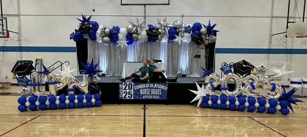 Blue, silver, and white balloon stage décor with Class of 2025 numbers, stars, and graduation caps by Party Perks STL for a nursing school graduation.