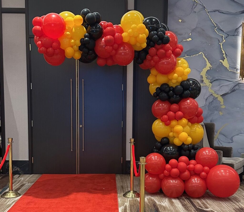 Red, yellow, and black organic balloon demi arch framing a red carpet entrance at a St. Louis event, created by Party Perks