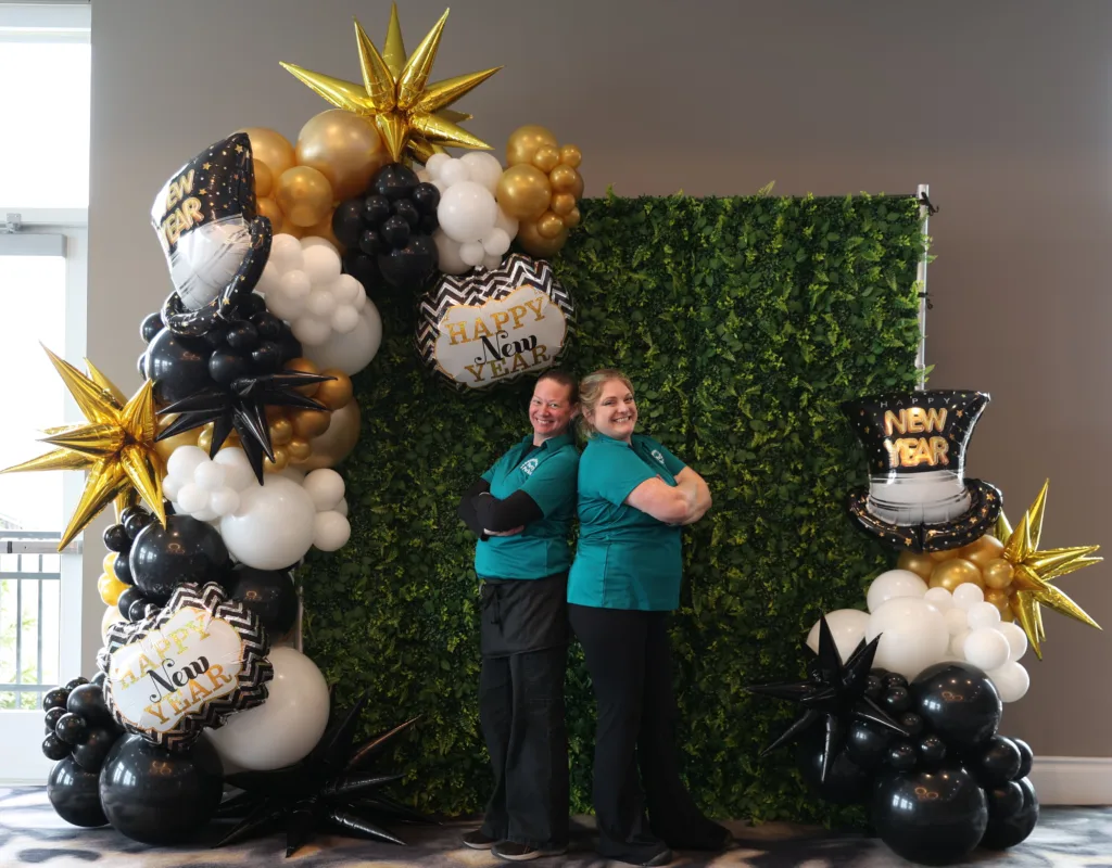 New Year’s Eve photo backdrop with greenery wall, gold starburts, black and white balloon clusters, and themed NYE foils by Party Perks STL.
