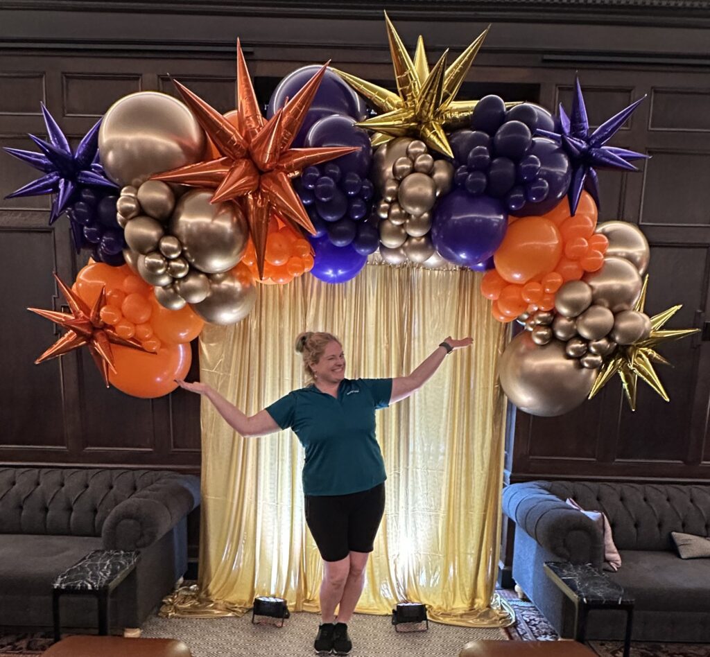 Purple, orange, and gold organic balloon arch with metallic starbursts over a gold backdrop for a luxury event by Party Perks