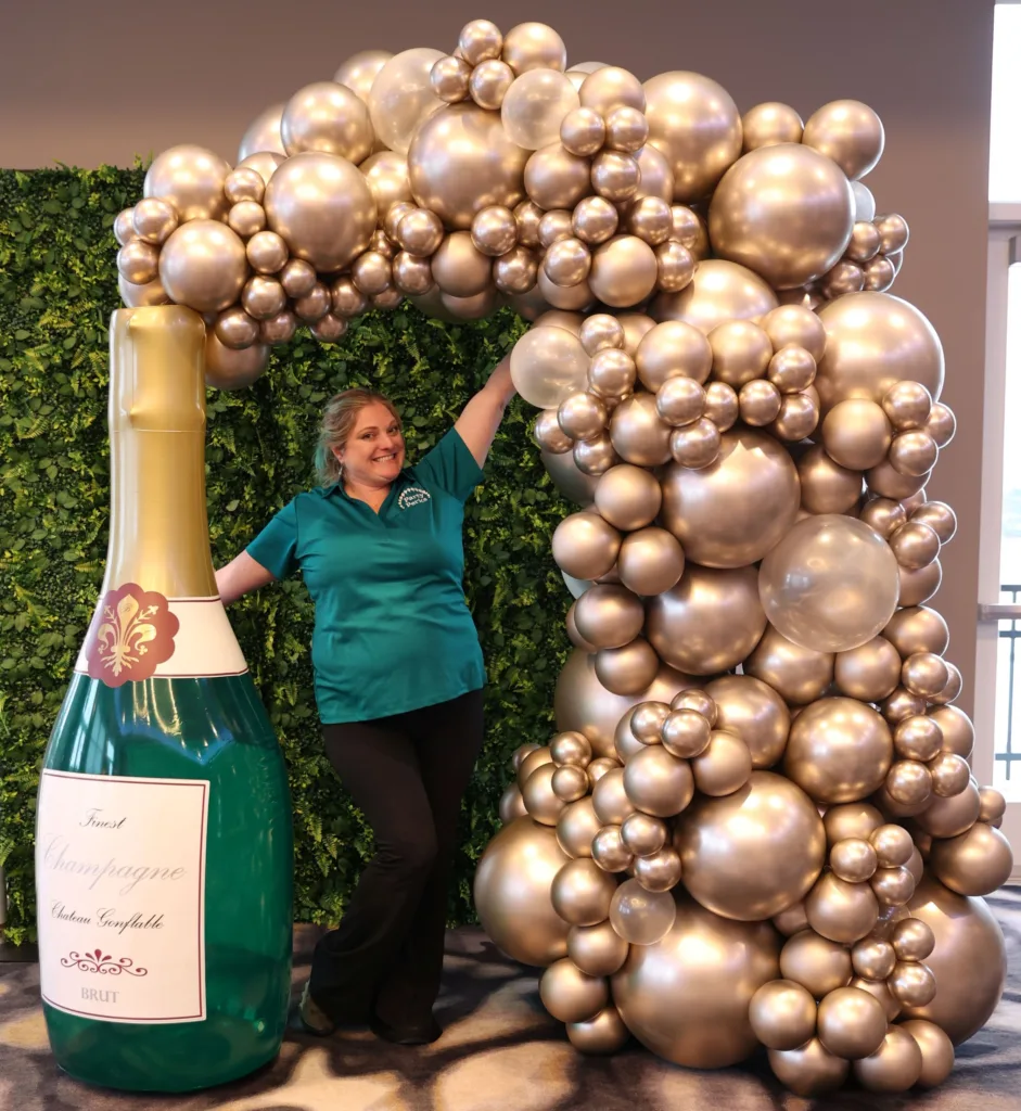 Luxury champagne bottle balloon photo op with gold organic balloon garland and greenery backdrop for New Year’s Eve décor in St. Louis.