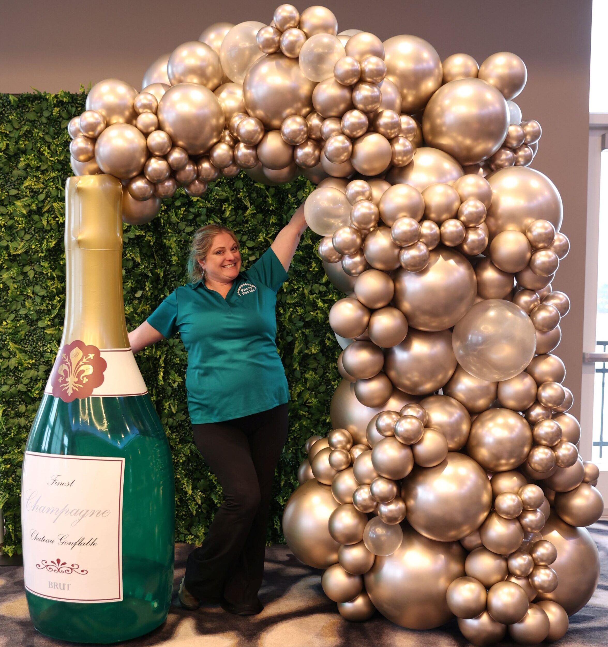 Luxury champagne bottle balloon photo op with gold organic balloon garland and greenery backdrop for New Year’s Eve décor in St. Louis.