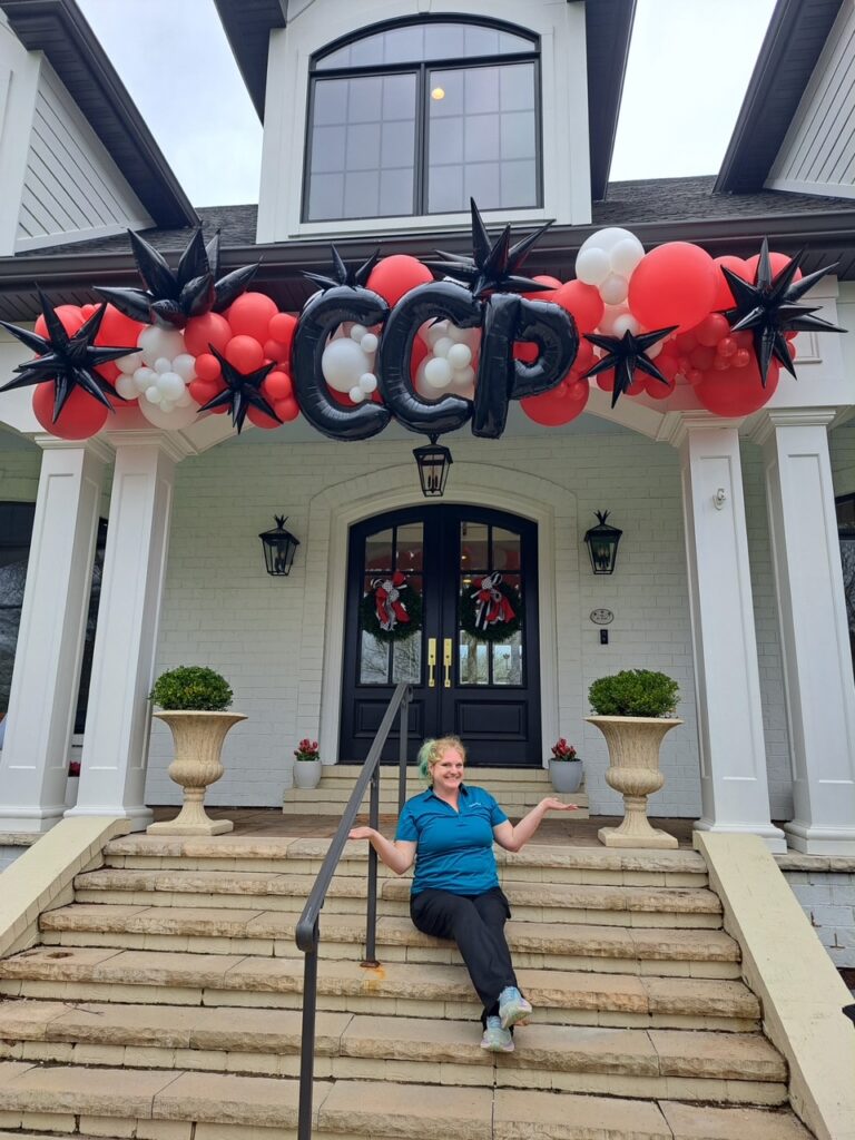Red, white, and black organic balloon garland with custom CCP letters and black starburst accents installed on a home entry by Party Perks