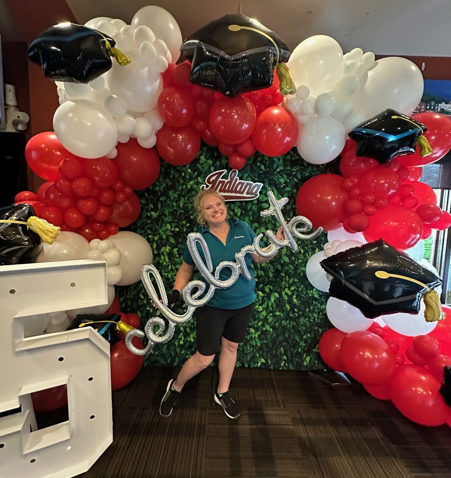 Graduation balloon backdrop in St. Louis featuring red and white custom balloon decor with graduation cap balloons and photo-ready greenery wall.
