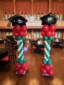 Graduation balloon columns in St. Louis featuring red, green, and white spiral design with oversized graduation cap toppers for university ceremony.