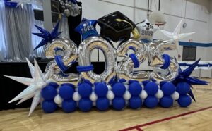 School graduation stage decor in St. Louis with 2025 balloon numbers, graduation cap accents, and blue and silver balloon base installation.