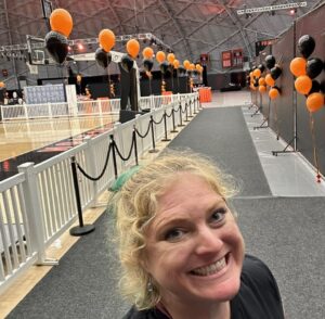 University graduation ceremony decor with black and orange helium balloon displays lining gymnasium walkway for large graduation event.