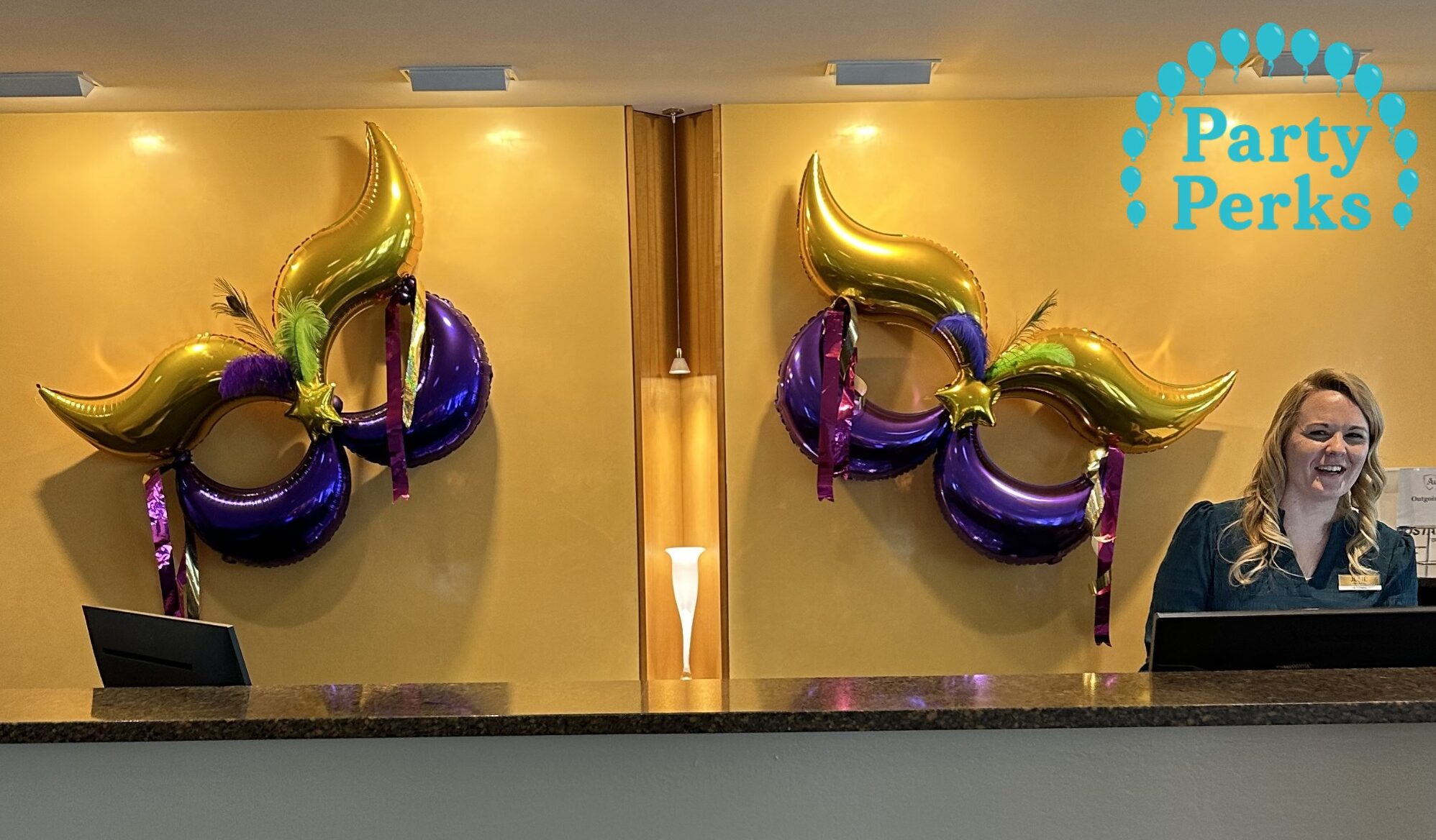 Mardi Gras balloon decorations with purple, gold, and green masks displayed behind an event reception desk in St. Louis.